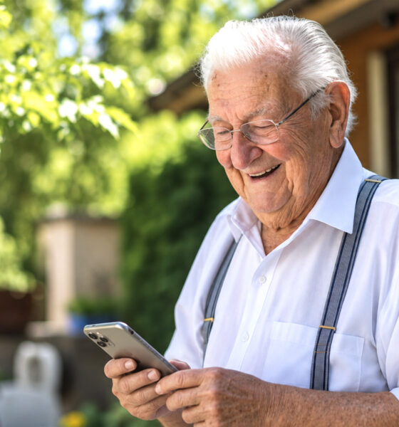 Stariji muškarac sa smiješkom čita poruke na mobitelu u vrtu.
