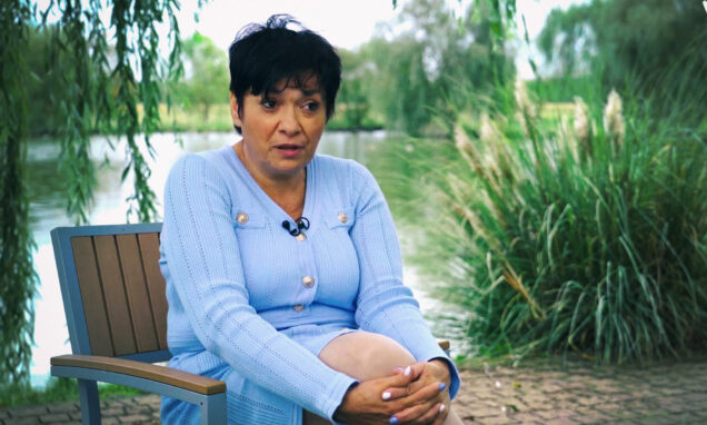 Bahra Zahirović sjedi na klupi uz jezero, u svijetloplavoj haljini, tijekom razgovora u prirodnom okruženju.