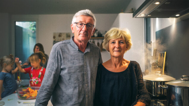 Bračni par u 60-ima stoji u kuhinji i gleda u kameru, dok se u pozadini para diže iz lonaca, a unuci se veselo igraju i pomažu u pripremi hrane. Obiteljska atmosfera puna topline i svakodnevne radosti.