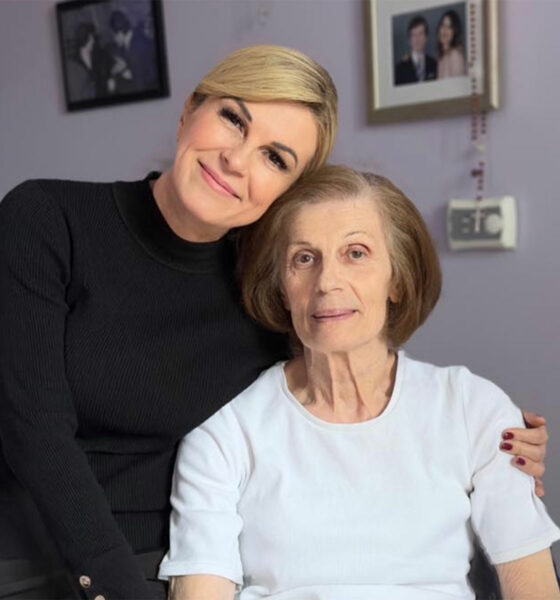 Kolinda Grabar-Kitarović sjedi zagrljena sa svojom majkom Dubravkom u toplom i intimnom okruženju doma. Oboje su nasmiješene i zrače bliskošću. Zid iza njih ukrašen je obiteljskim fotografijama, stvarajući ugođaj obiteljske ljubavi i zajedništva.