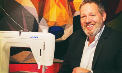 Mike O'Dell, osnivač tvrtke Legit Kits, sjedi uz šivaći stroj ispred šarenog geometrijskog quilt uzorka – portret uspješnog poduzetnika iz svijeta kreativnog šivanja.