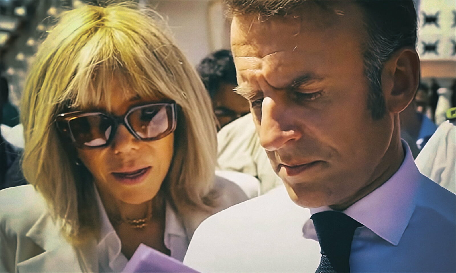 Francuski predsjednik Emmanuel Macron i njegova supruga Brigitte Macron u zajedničkom javnom nastupu, fokusirani na dokument tijekom službenog događanja na otvorenom.