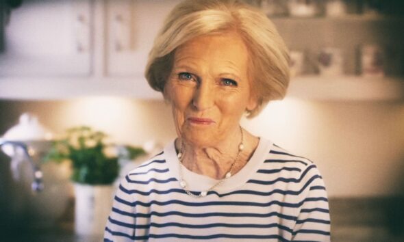 Mary Berry stoji u kuhinji, odjevena u bijelu majicu s plavim prugama, s blagim osmijehom na licu.