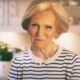 Mary Berry stoji u kuhinji, odjevena u bijelu majicu s plavim prugama, s blagim osmijehom na licu.