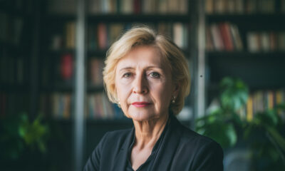 Starija žena u tamnom sakou stoji ispred police s knjigama.