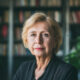 Starija žena u tamnom sakou stoji ispred police s knjigama.