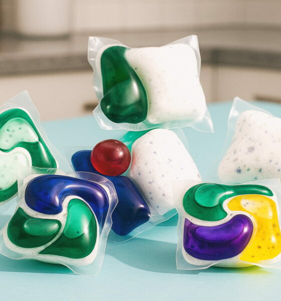 Raznobojne kapsule i tablete za perilicu posuđa na plavoj podlozi u kuhinji.