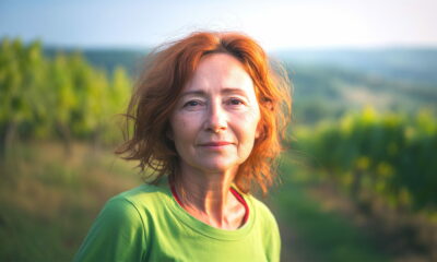 Žena s crvenkastom kosom u zelenoj majici stoji u vinogradu u Istri, iza nje se proteže prirodni krajolik u zlatnom svjetlu zalaska.
