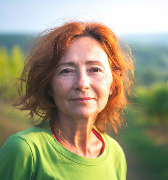 Žena s crvenkastom kosom u zelenoj majici stoji u vinogradu u Istri, iza nje se proteže prirodni krajolik u zlatnom svjetlu zalaska.