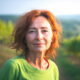 Žena s crvenkastom kosom u zelenoj majici stoji u vinogradu u Istri, iza nje se proteže prirodni krajolik u zlatnom svjetlu zalaska.