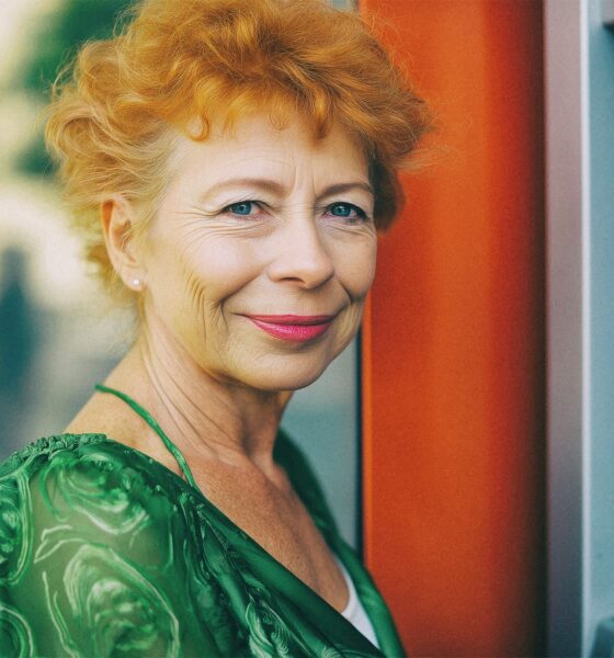 Starija žena u zelenoj haljini nasmiješeno stoji pokraj bankomata.