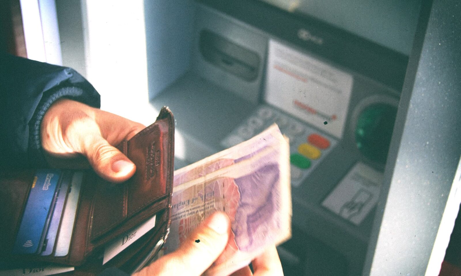 Osoba u ruci drži novčanik s novčanicama, podiže novac s bankomata.
