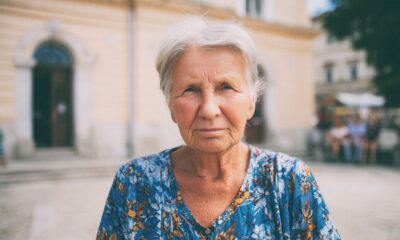 Portret žene sa svijetlom kosom i šalom ispred crkve, gleda prema gore u sunčanom danu.