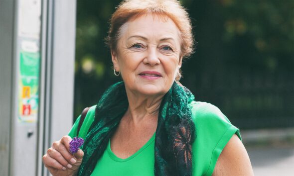 Starija žena u zeleno majici gleda u kameru.