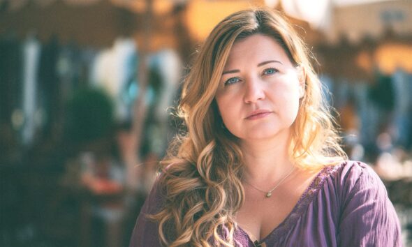 Mlada žena duge kose i plavih očiju sjedi u kafiću.