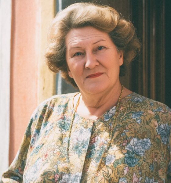Starija žena sa staromodnom frizurom stoji na vratima obiteljske kuće.