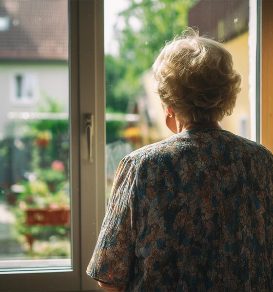 Starija žena gleda kroz prozor obiteljske kuće.