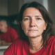 Žena u crvenoj majici sjedi u kuhinji i proučava dokumente o mirovini.