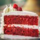 Kriška torte red velvet na bijelom tanjuru ukrašena šlagom i malinama.
