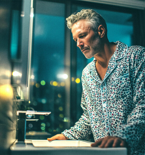 Muškarac naslonjen na umivaonik u kupaonici.