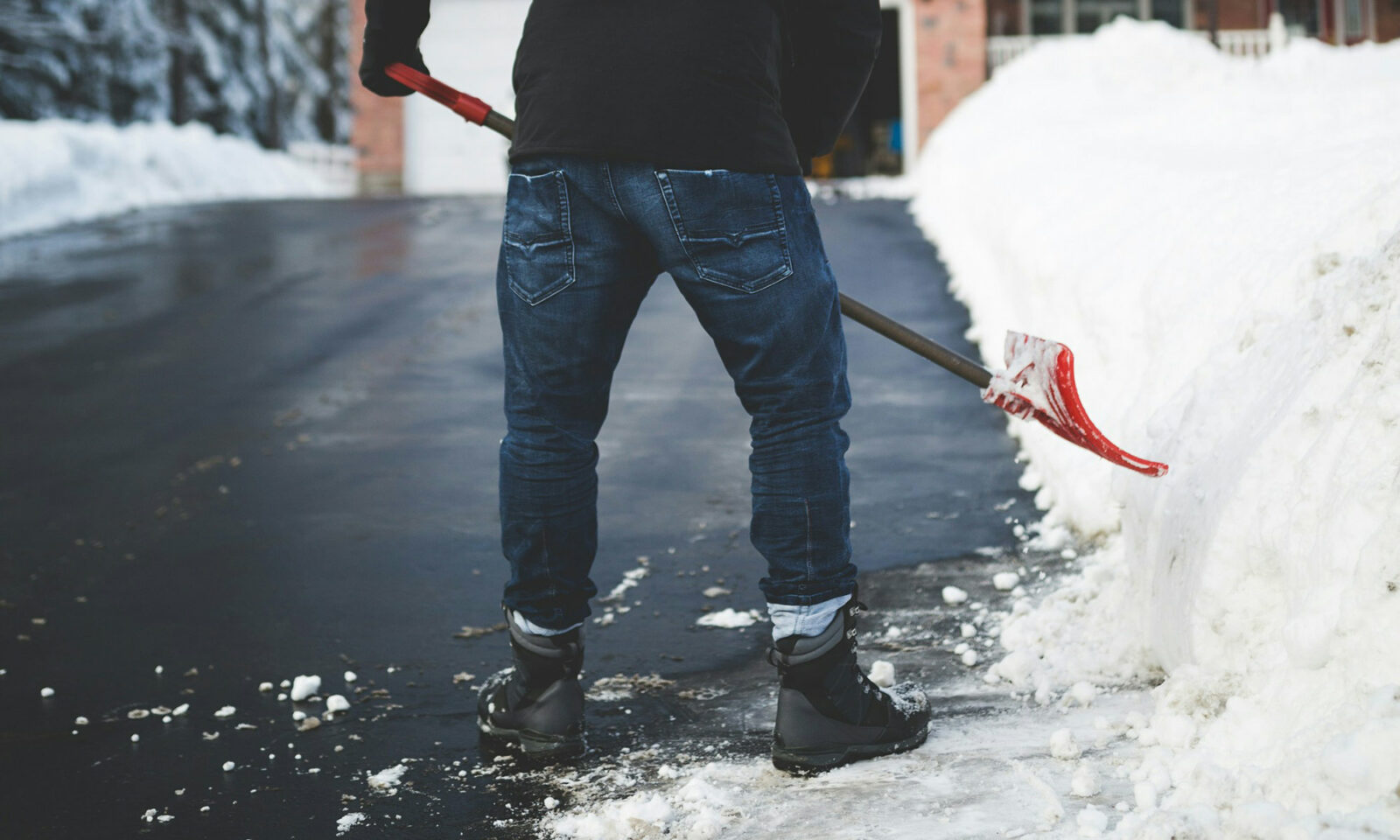 Muškarac čisti snijeg na prilazu kući.