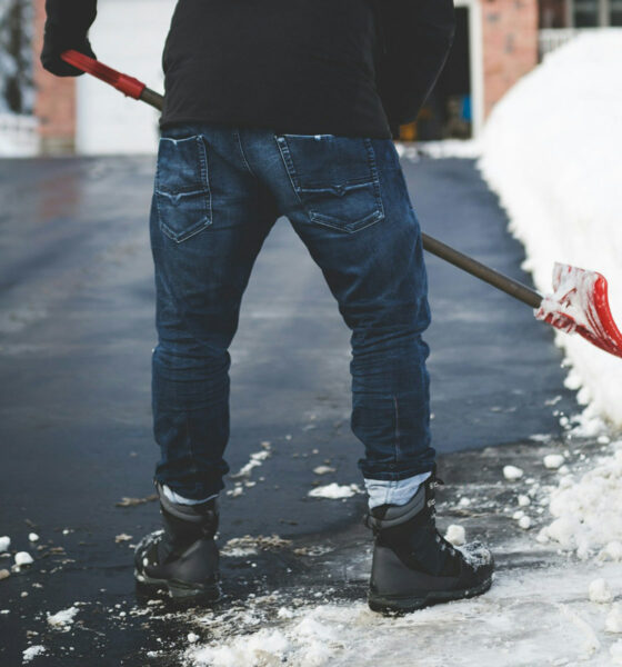 Muškarac čisti snijeg na prilazu kući.