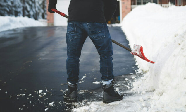 Muškarac čisti snijeg na prilazu kući.