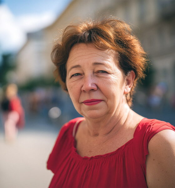 žena u crvenom topu na naramenice stoji na zagrebačkoj ulici i gleda u kameru.