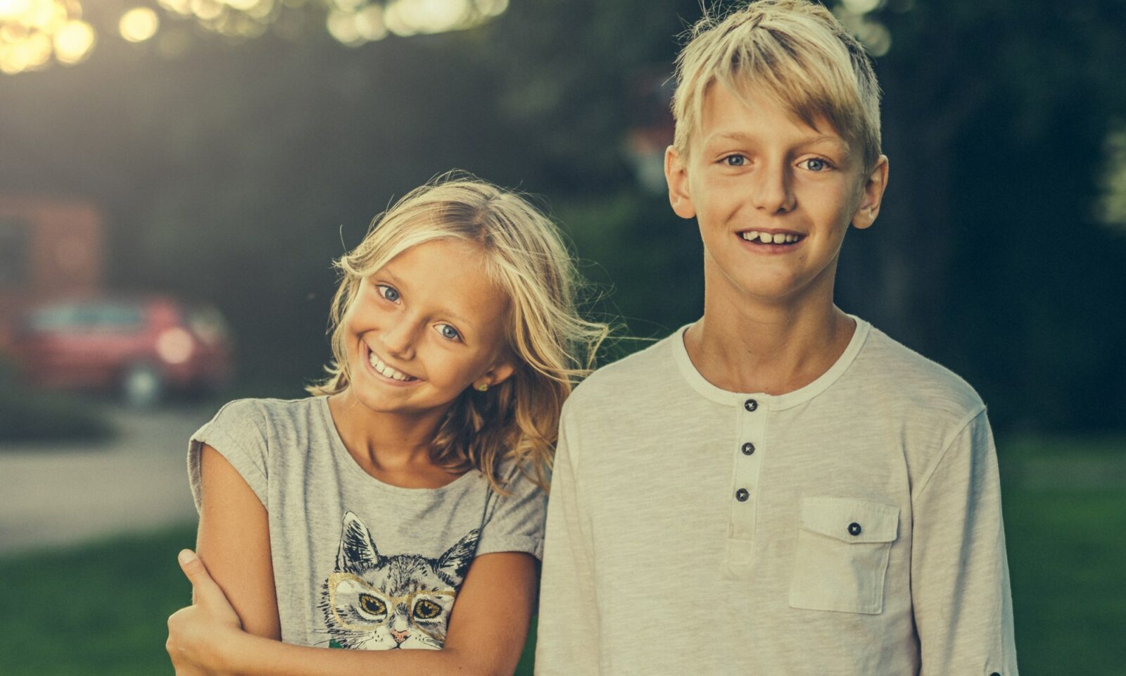 Djevojčica i dječak obasjani večernjim suncem gledaju u kameru.