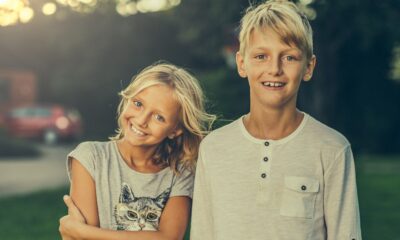 Djevojčica i dječak obasjani večernjim suncem gledaju u kameru.