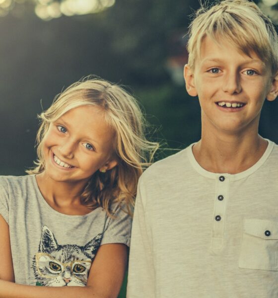 Djevojčica i dječak obasjani večernjim suncem gledaju u kameru.