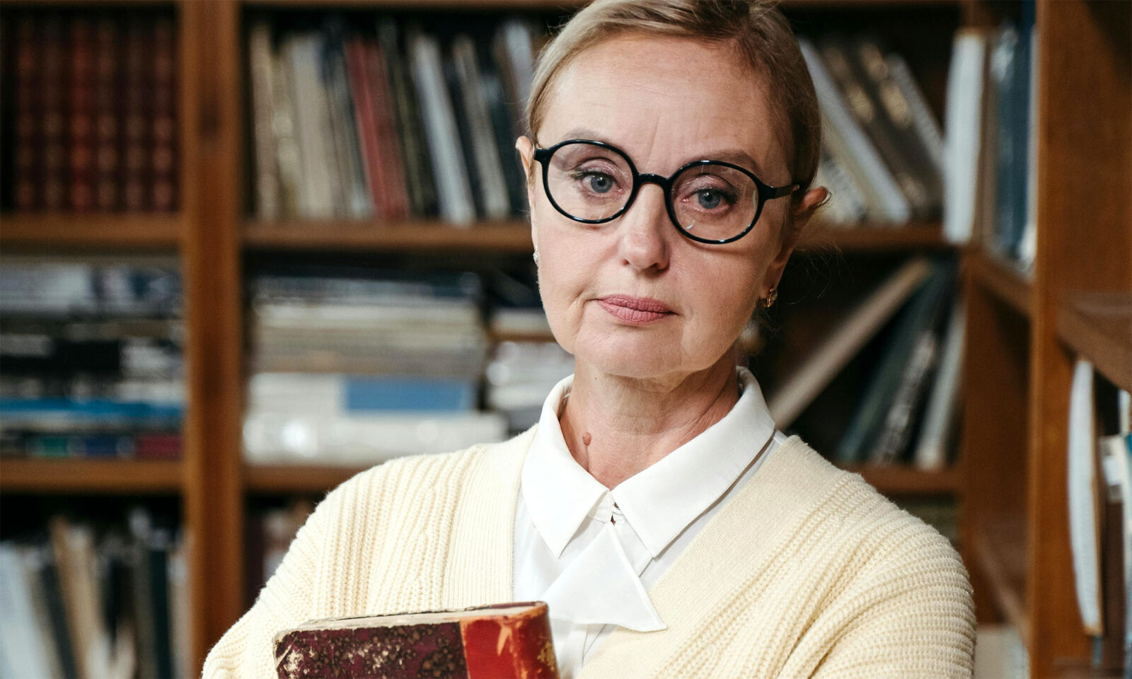Žena s naočalama i knjigom u biblioteci.