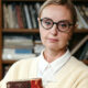 Žena s naočalama i knjigom u biblioteci.