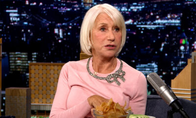 Helen Mirren u ružičastoj majici tijekom gostovanja u televizijskoj emisiji, s mikrofonom i zdjelom čipsa ispred sebe.