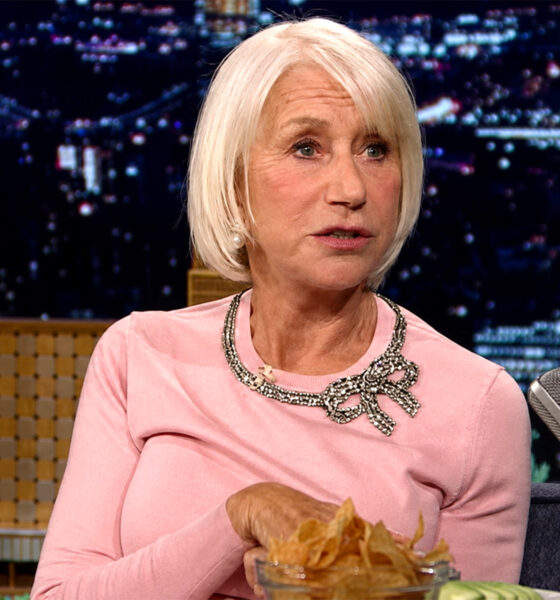Helen Mirren u ružičastoj majici tijekom gostovanja u televizijskoj emisiji, s mikrofonom i zdjelom čipsa ispred sebe.