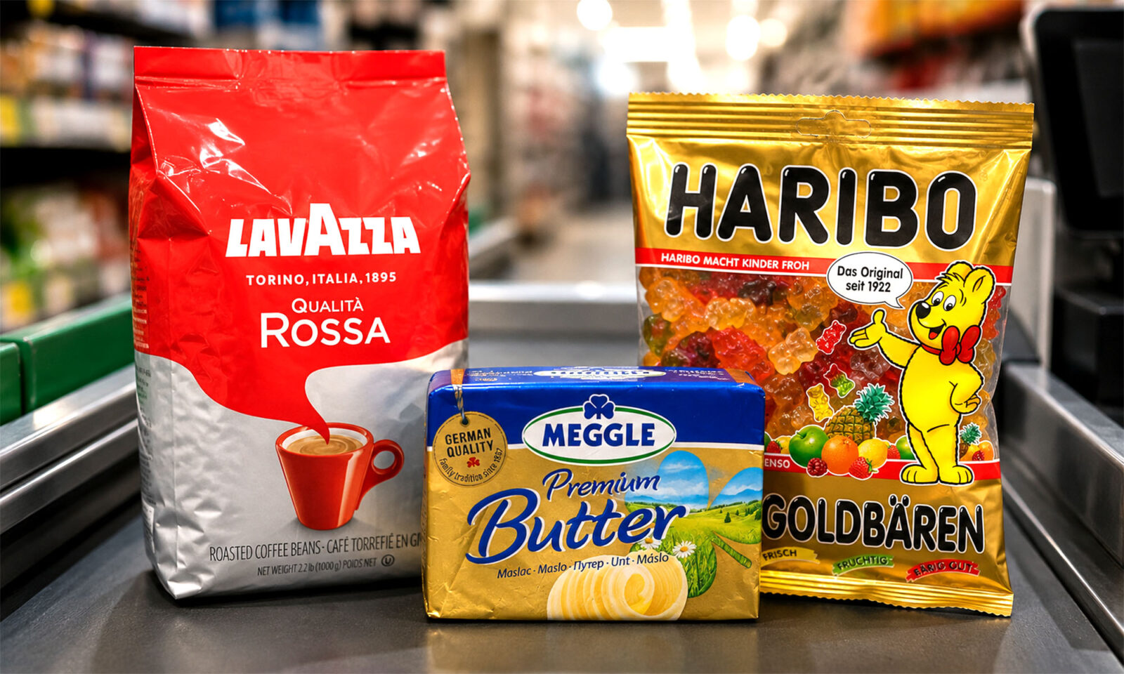Na blagajni supermarketa uz zamućenu pozadinu trgovine stoje tri proizvoda čije se cijene uspoređuju: Lavazza Qualità Rossa kava u zrnu, Haribo Zlatni medo gumeni bomboni i Meggle Premium maslac.