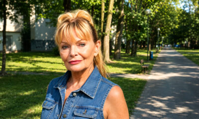 Starija žena u traper-prsluku stoji na osunčanoj zagrebačkoj šetnici okruženoj zelenilom, klupama i stambenim zgradama.