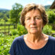 Starija žena stoji u sunčanom vrtu u Gorskom kotaru, okružena zelenilom, povrtnjakom i ruralnim krajolikom.