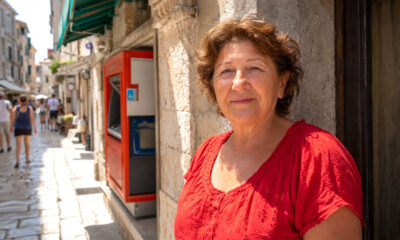 Žena u crvenoj ljetnoj bluzi zadovoljno se smiješi pokraj bankomata u središtu Pule.
