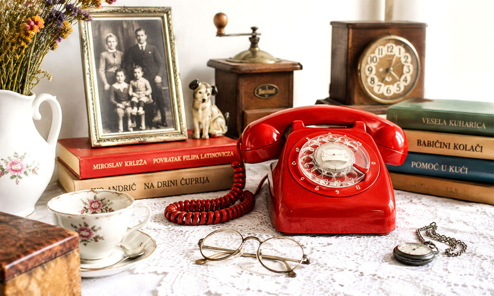 Stari obiteljski predmeti, fotografija, knjige, porculan i crveni telefon na stolu u hrvatskom domu.