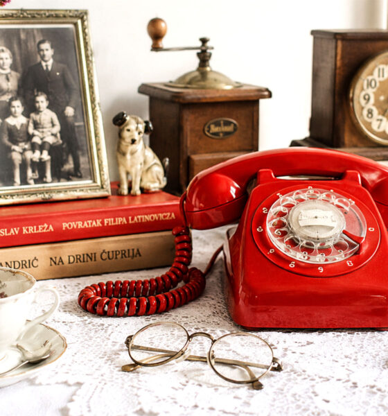 Stari obiteljski predmeti, fotografija, knjige, porculan i crveni telefon na stolu u hrvatskom domu.