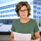 Žena u zelenoj majici drži mirovinske dokumente i gleda u kameru, dok se iza nje na ekranu vidi zgrada HZMO-a.