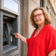 Starija žena u crvenoj bluzi i s crvenim naočalama koristi bankomat u središtu Zagreba.