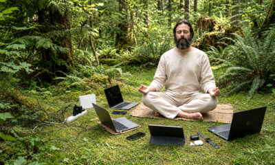Bradati guru meditira u šumi okružen laptopima, mobitelima, routerom, punjačima i kabelima.