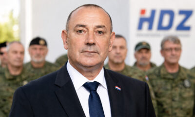 Ministar Tomo Medved ispred hrvatskih branitelja u maskirnim odorama i zamućenog logotipa HDZ-a.