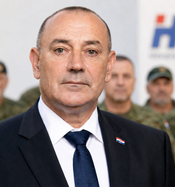 Ministar Tomo Medved ispred hrvatskih branitelja u maskirnim odorama i zamućenog logotipa HDZ-a.
