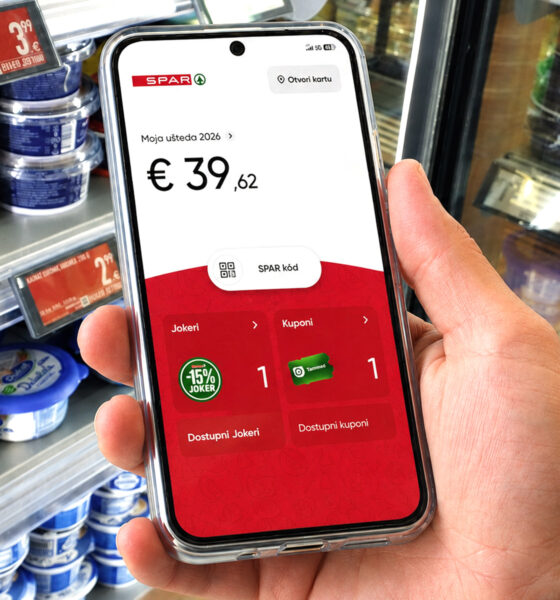 Kupac u trgovini drži mobitel s otvorenom aplikacijom SPAR programa vjernosti, prikazom uštede, kupona i Jokera.