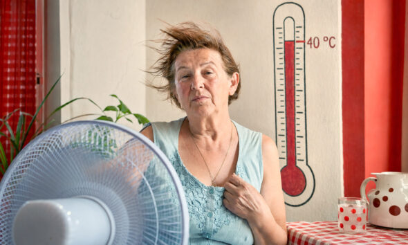 Starija žena rashlađuje se pred ventilatorom u stanu, dok termometar iza nje pokazuje 40 Celzijevih stupnjeva.