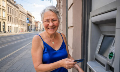 Starija žena u kraljevski plavoj svilenoj bluzi drži karticu pokraj bankomata u zagrebačkoj Ilici.