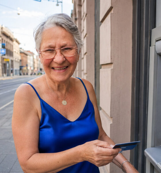 Starija žena u kraljevski plavoj svilenoj bluzi drži karticu pokraj bankomata u zagrebačkoj Ilici.
